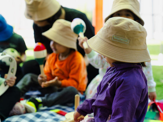 Children in sun hats share a tambourine and maracas on a picnic rug