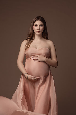ritratto di una mamma in dolce attesa con lunghi capelli color miele e occhi azzurri con un tessuto pastello pesca drappeggiato svolazzante ed etereo dallo stile contemporaneo glamour fashion editoriale raffinato e ricercato che celebra la femminilità e curve della sua maternità e gravidanza