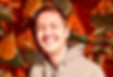 Smiling man in gray hoodie, autumn leaf background