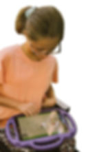 Girl in a pink shirt uses a tablet as AAC device with a purple case, displaying icons. She sits in a chair, focused and engaged. White background.