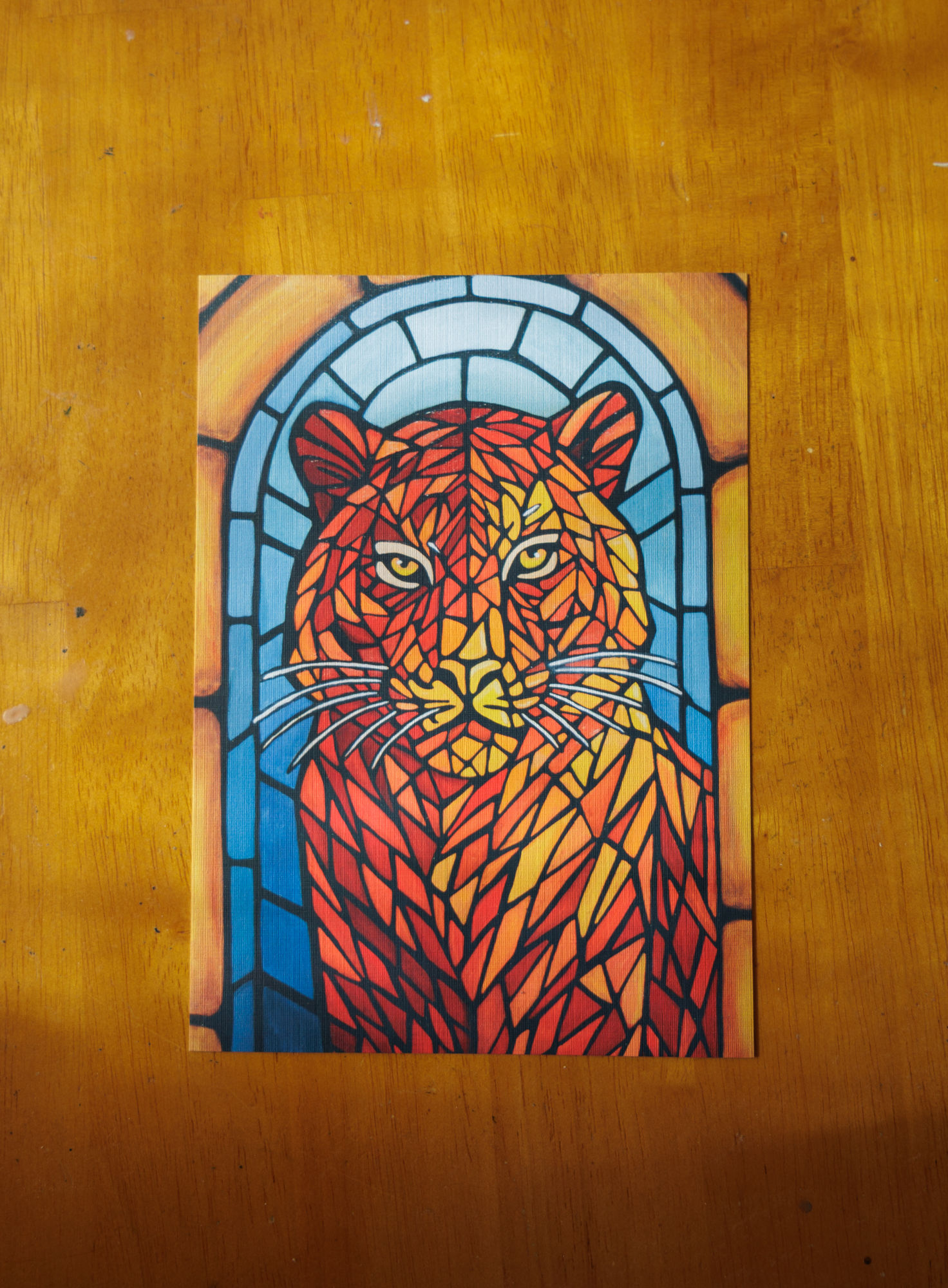 red, orange, and yellow stained glass tiger in front of a blue stained glass arch surrounded by yellow stones