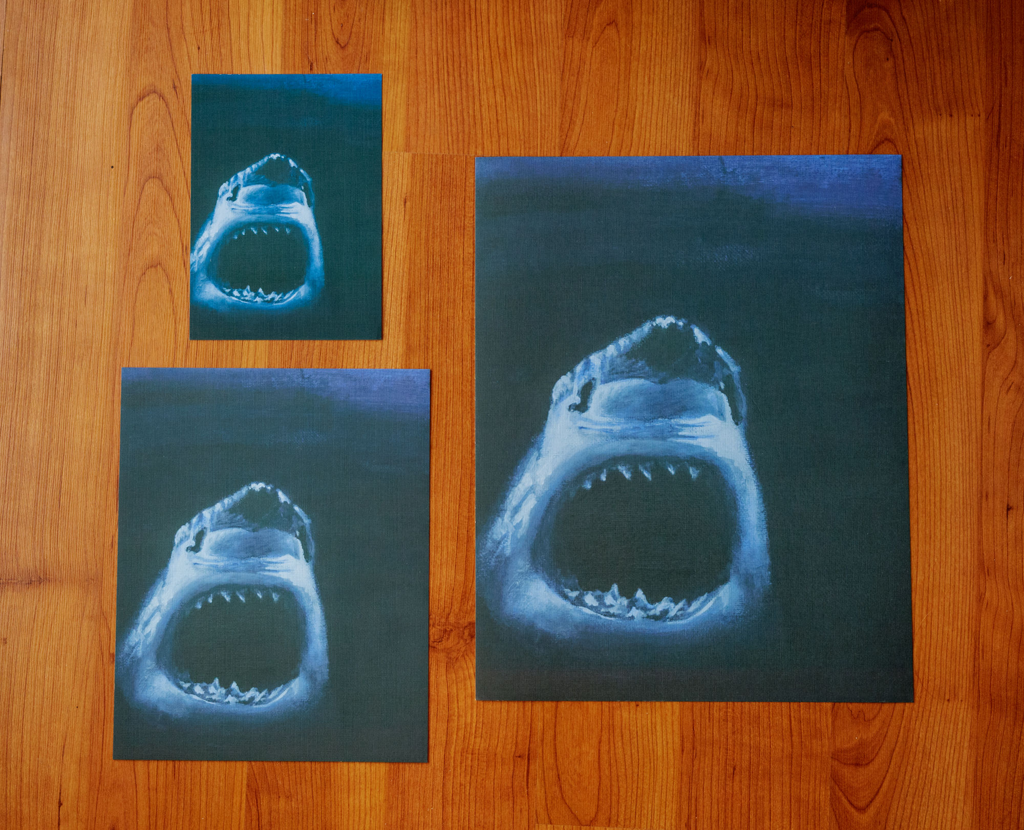 three sizes of prints of a blue shark coming out of the darkness