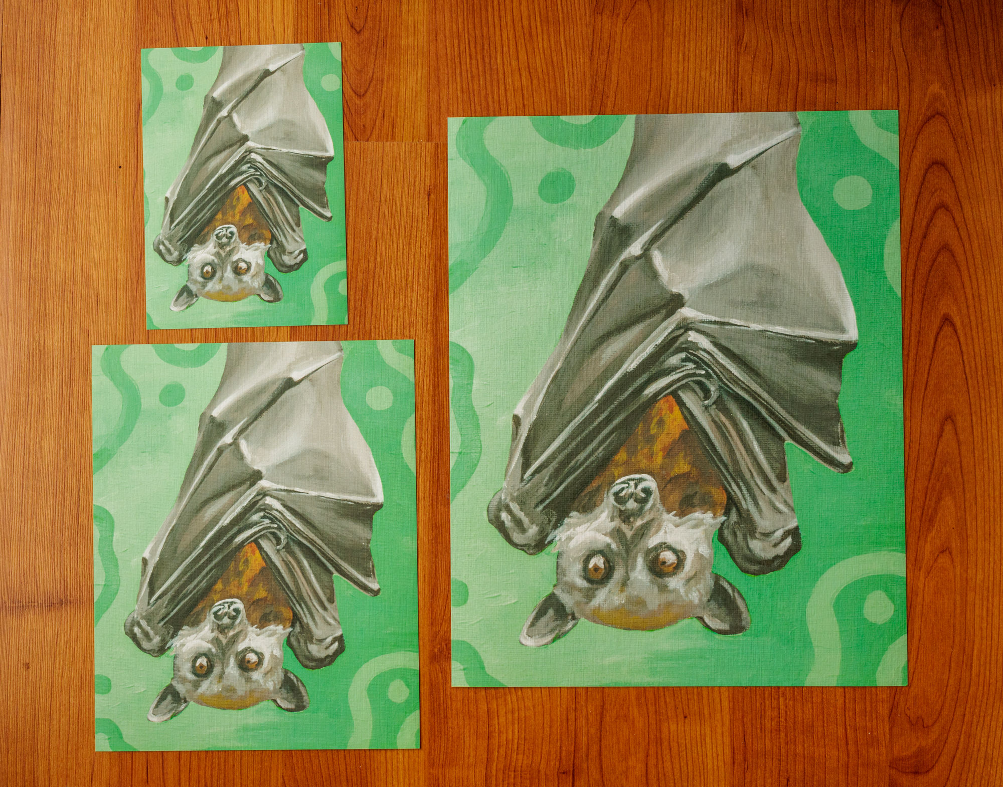 three sizes of prints of an orange and gray bat in front of a green background with dots and squiggles