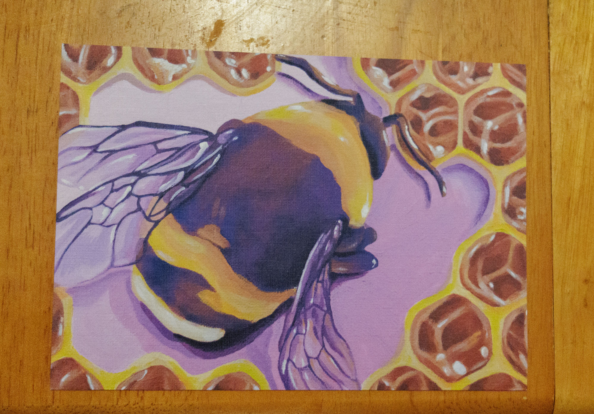 print of yellow and purple bumblebee surrounded by honeycomb and a purple background, on a table
