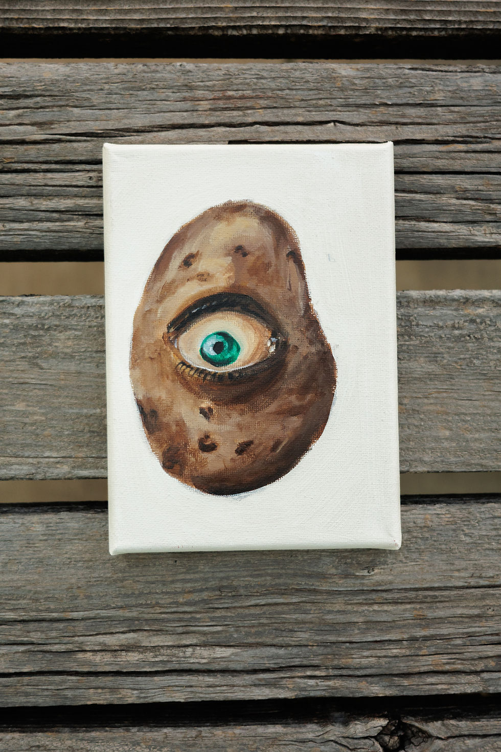 Thumbnail: painting of a russet potato with a teal eyeball looking at you, sitting on wood