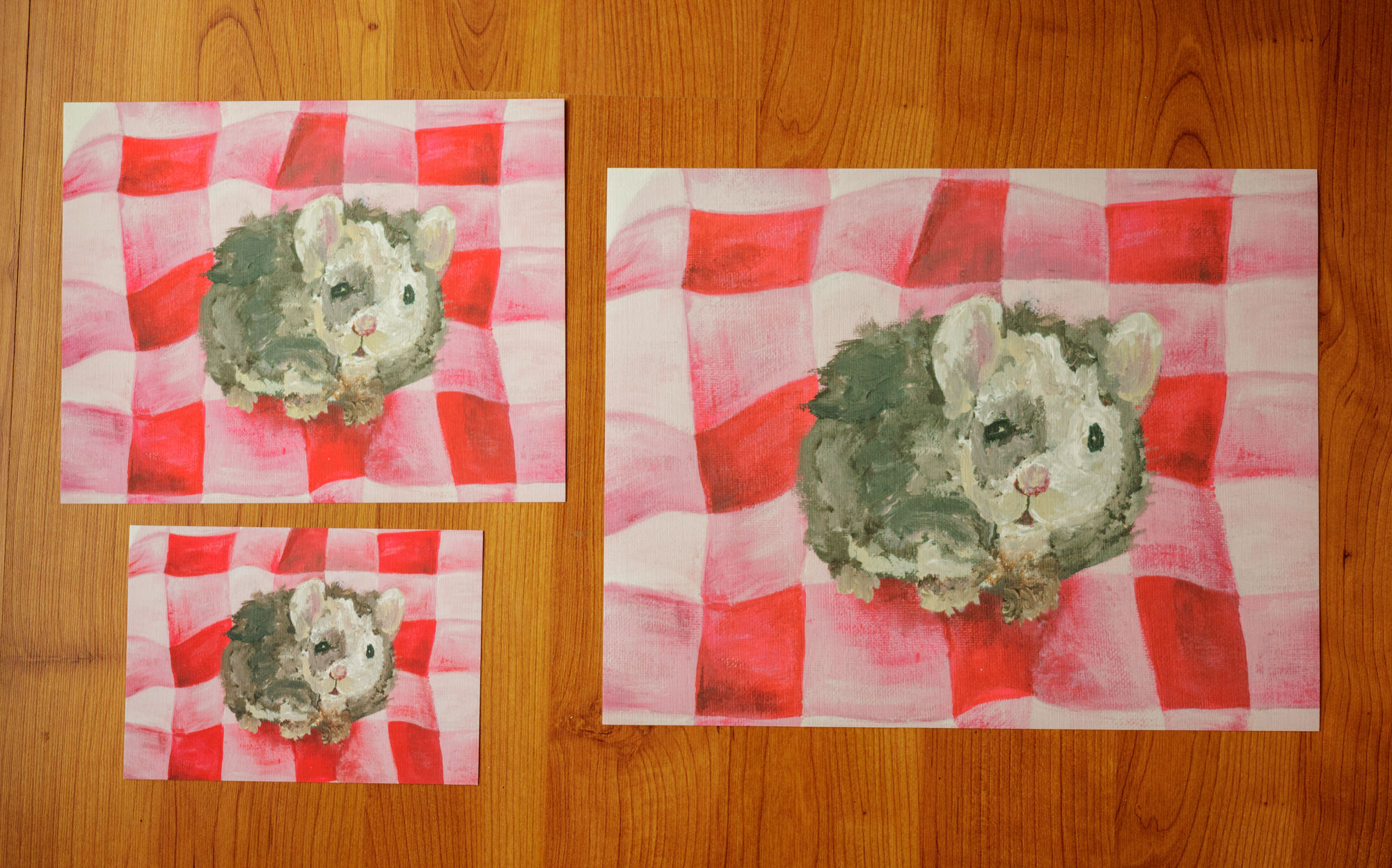 three sizes of prints of a brown and cream mouse on a red, pink, and light pink gingham blanket