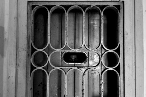 a black and white photo of a man peeking through a fence