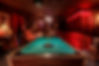 Speakeasy themed room with mood lighting, billiard table, photos on the wall, red velvet curtains, antique furniture