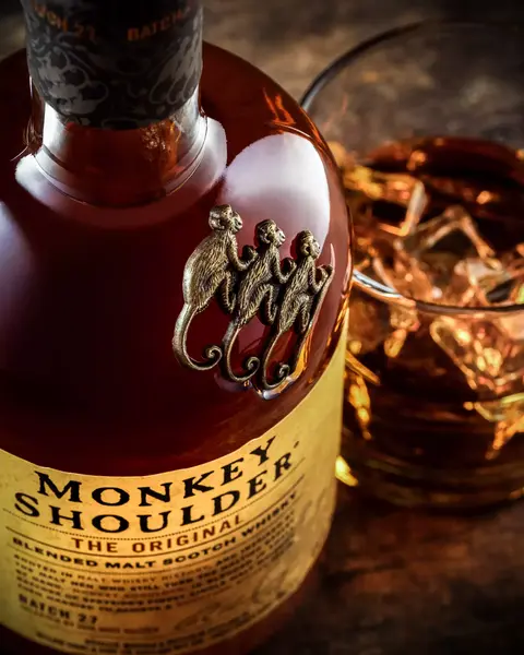 Detail shot of the iconic three-monkey emblem on a whisky bottle with amber liquid in the background