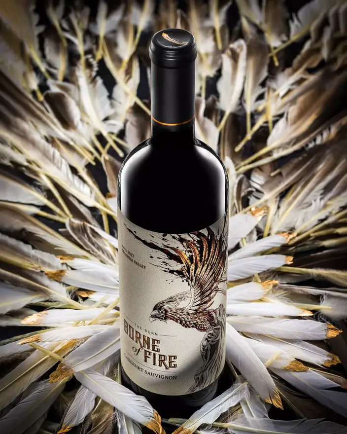Artistic wine photography featuring a bird-themed label surrounded by white feathers