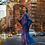 Thumbnail: A woman in a vibrant purple and blue painted dress gracefully strolls along a bustling New York City street, surrounded by th