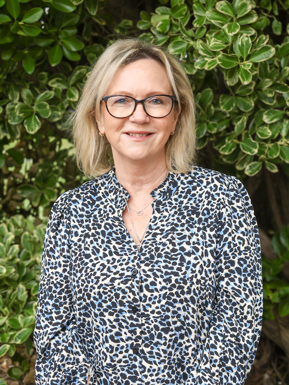Smiling picture of Trudie France Holistic cancer support with glasses in front of green foliage