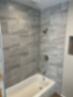 Modern bathtub with grey wood-look tiled walls.