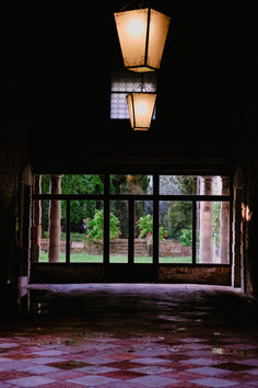 Interior of a dimly lit building with glowing yellow square lights hanging from the ceiling, purple tiled floor, and a window revealing a garden outside