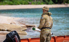 Australian Army soldier smiling while holding supplies in a dinghy on a beach in Vanuatu during humanitarian aid operations