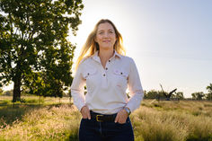 Portrait of a woman in country clothes standing on a farm at sunset with warm golden light illuminating the scene