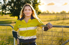 Woman wearing high-visibility workwear standing in a sunlit field at sunset on a farm.
