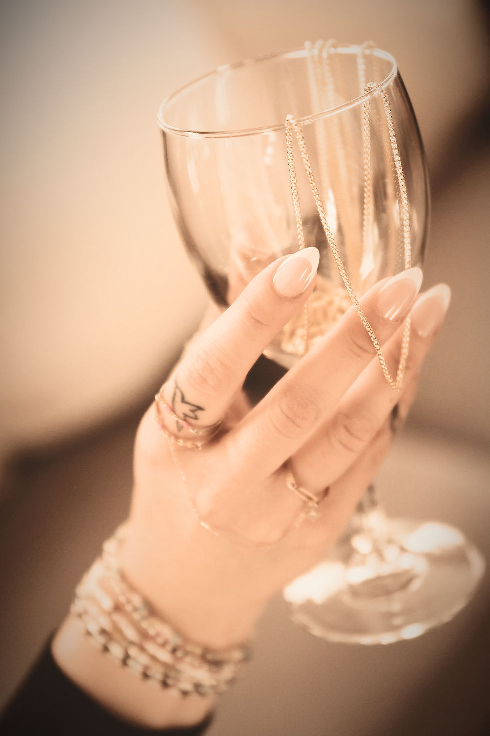 Woman holding a wine glass with permanent jewelry chains draped across it