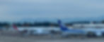 Planes from Emirates, ANA, and Air Canada parked at an airport with snowy mountains in the background. Terminal gates labeled S16, S1a.