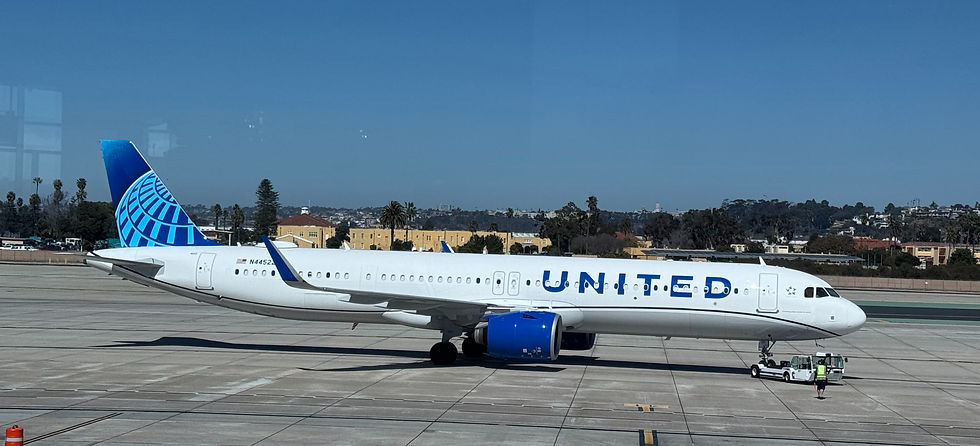 United jet on airport tarmac with tow vehicle and ground crew under a clear blue sky, white fuselage and blue tail/engine