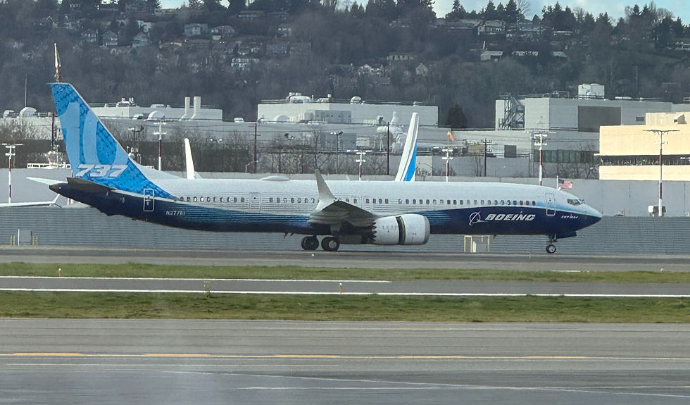 Blue Boeing 737 taxiing on a runway at an airport, with white buildings and hills in the background.