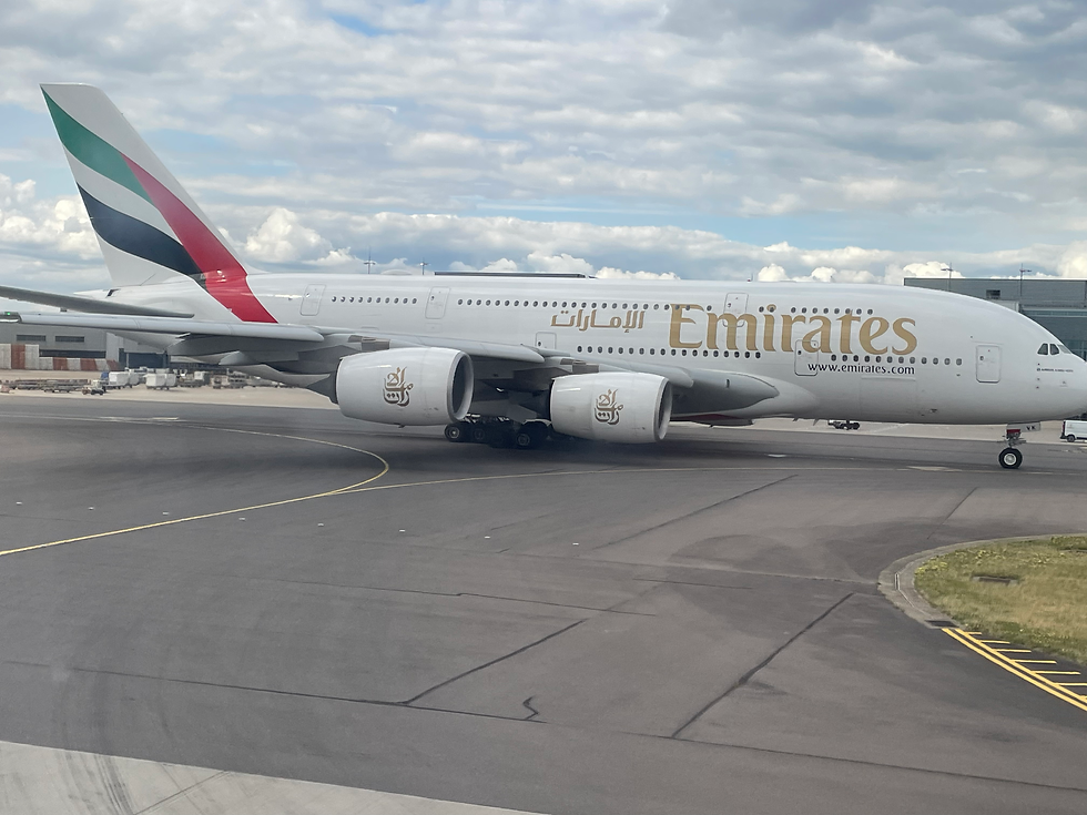 Emirates plane on tarmac under cloudy sky, with airline branding visible. The aircraft is stationary, set against an airport backdrop.