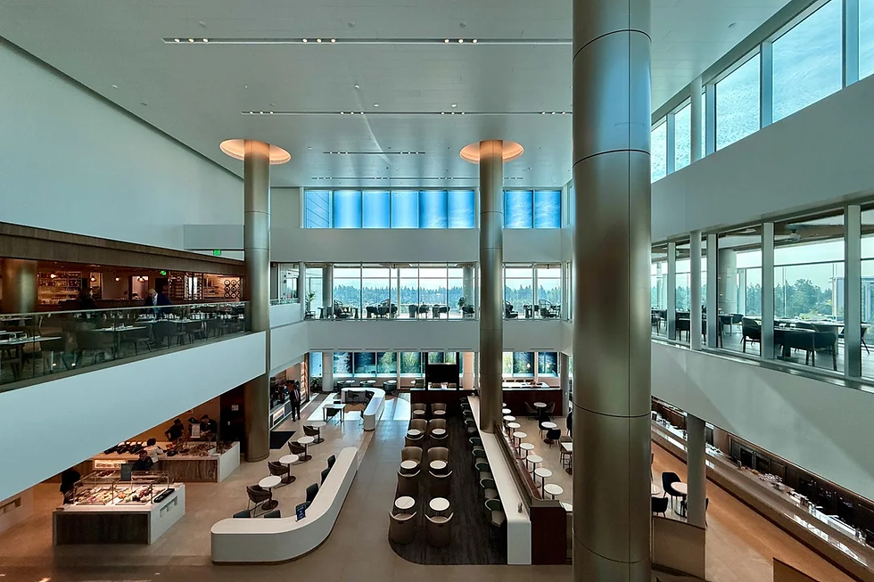 Spacious airport lounge with high ceilings, modern decor, and large windows. Empty tables and chairs, bar on the side, calm ambiance.