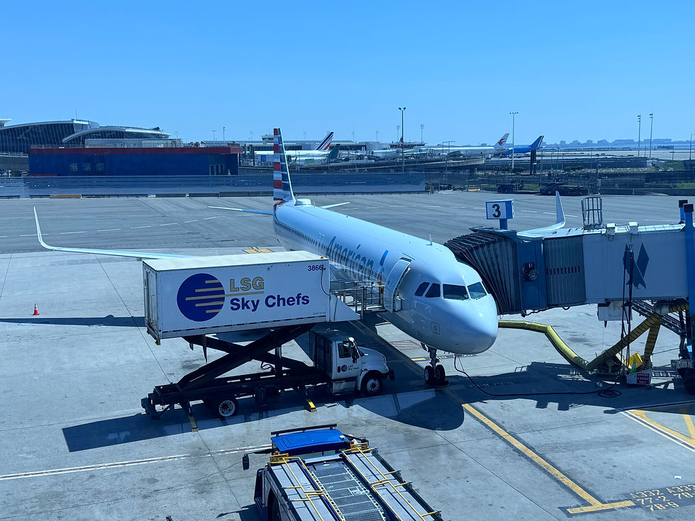 American Airlines jet at gate with LSG Sky Chefs truck and jet bridge on a sunny airport tarmac, blue sky above