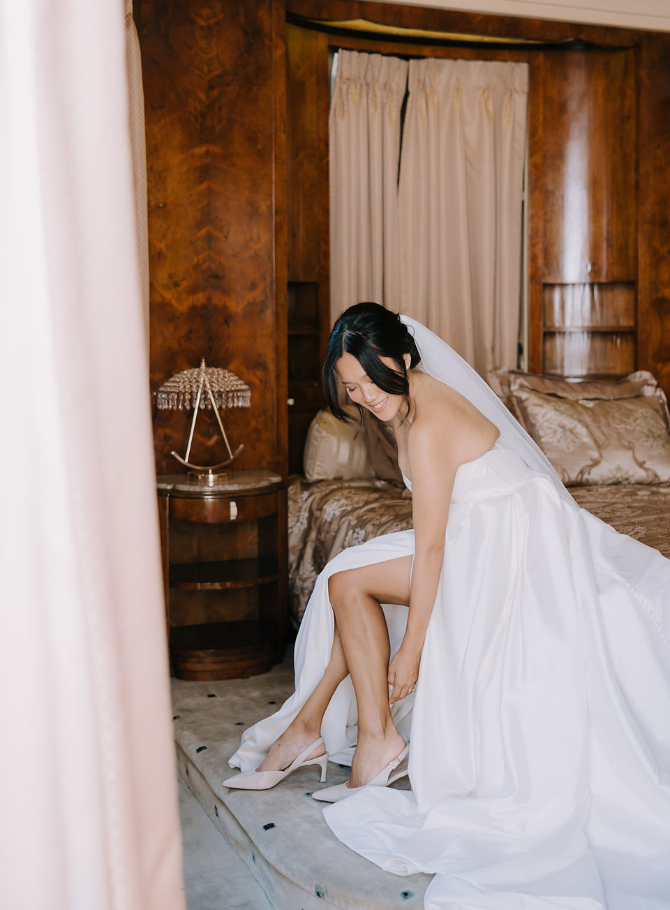Bride sitting on the edge of the bed in The Oviatt Penthouse as she puts on her wedding shoes.