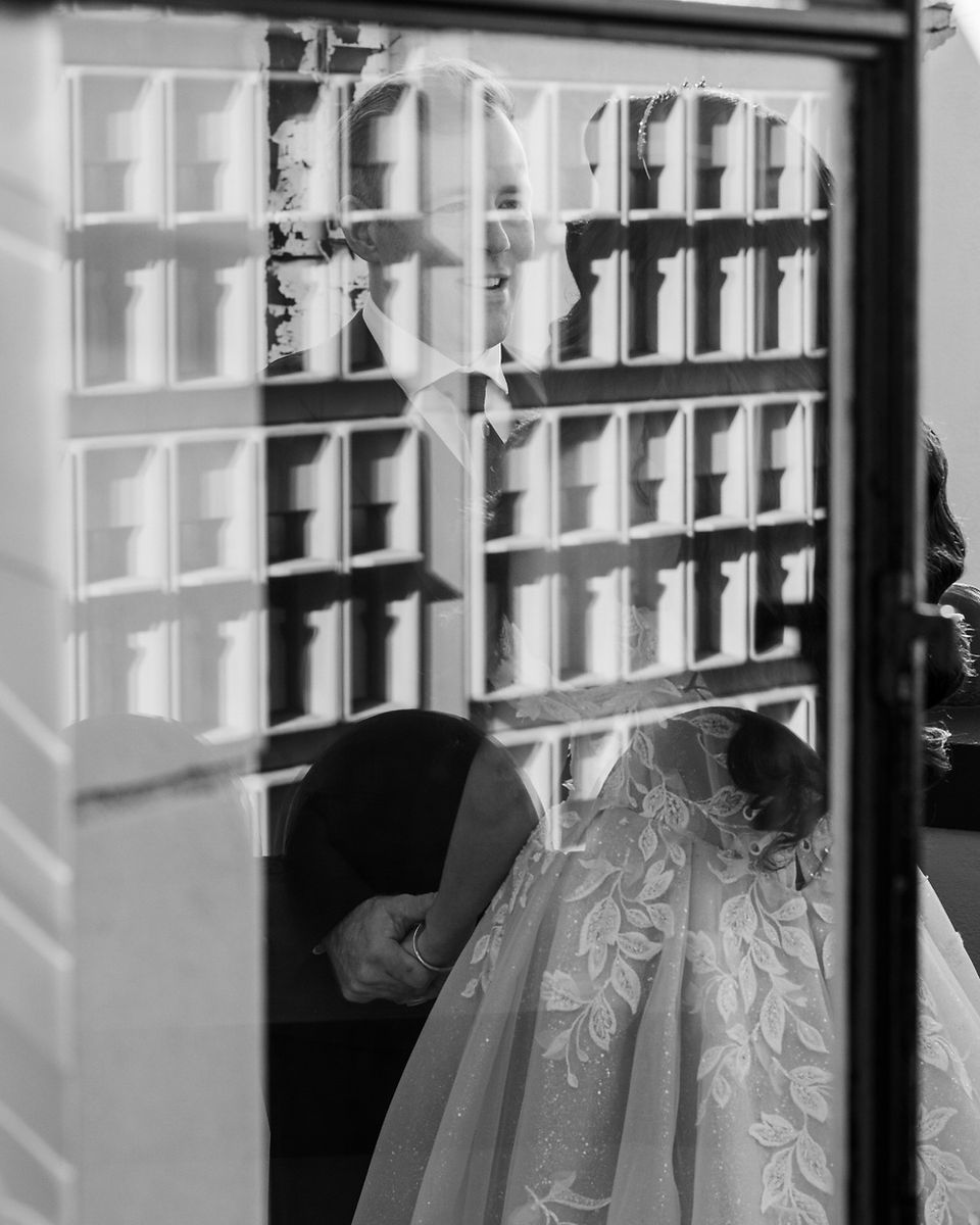 Bride and groom holding hands behind a glass window at The Oviatt.
