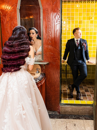 Bride and groom talking in The Oviatt’s Art Deco elevator lobby with yellow tiles.
