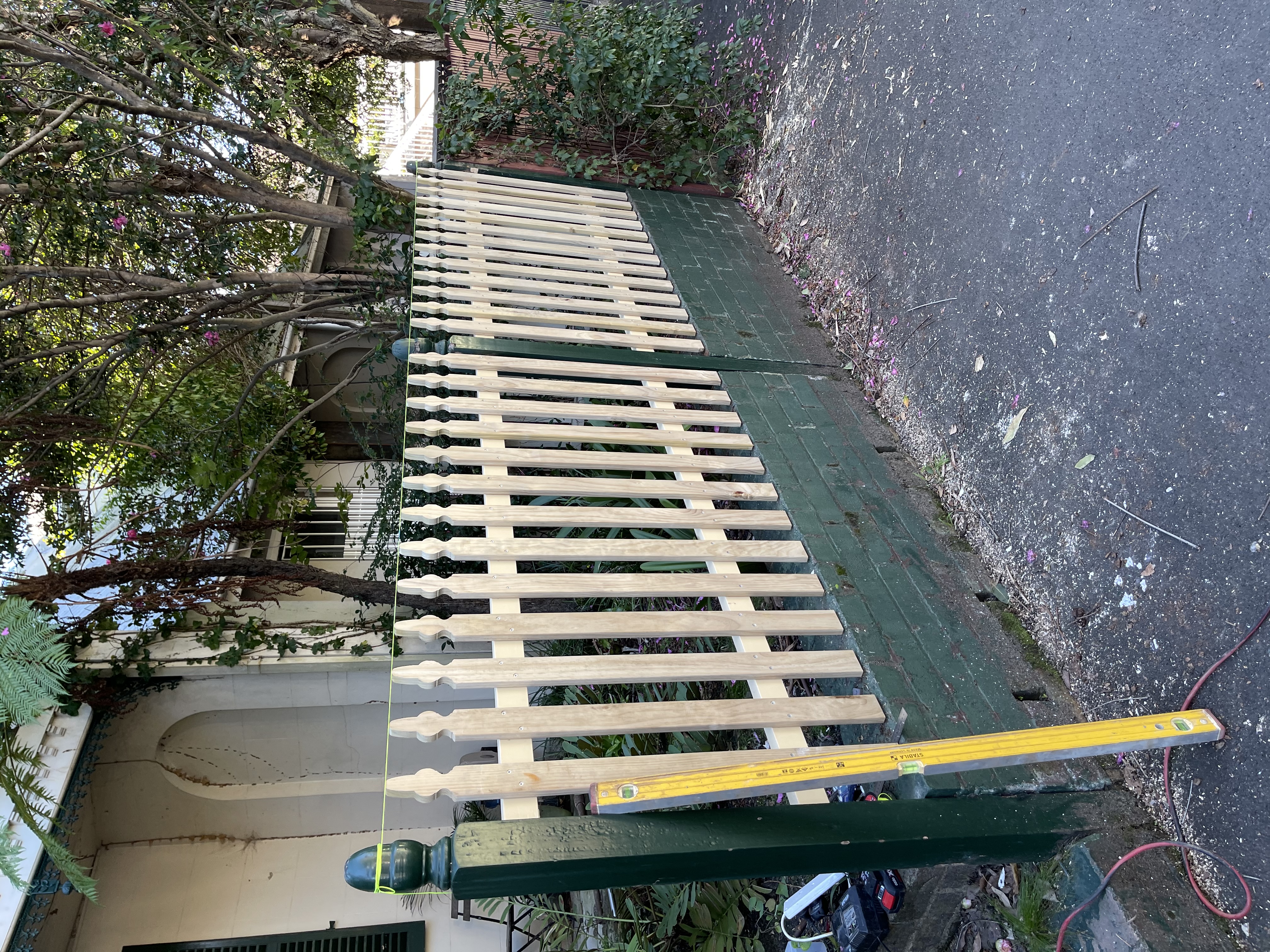 New unpainted timber picket fence being installed on a painted brick base, with tools on site