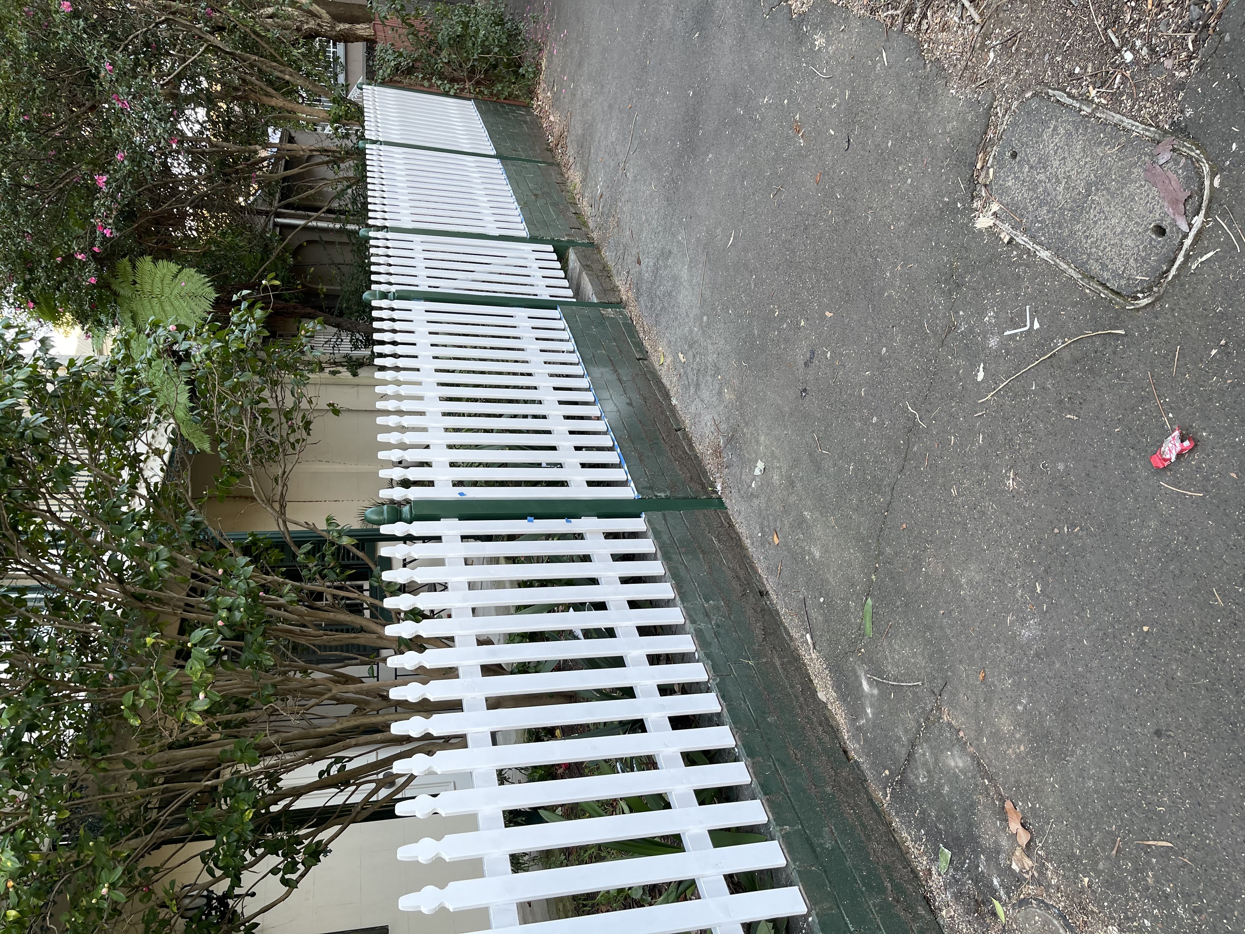 Finished white timber picket fence with pointed finials on a painted brick base, along a driveway