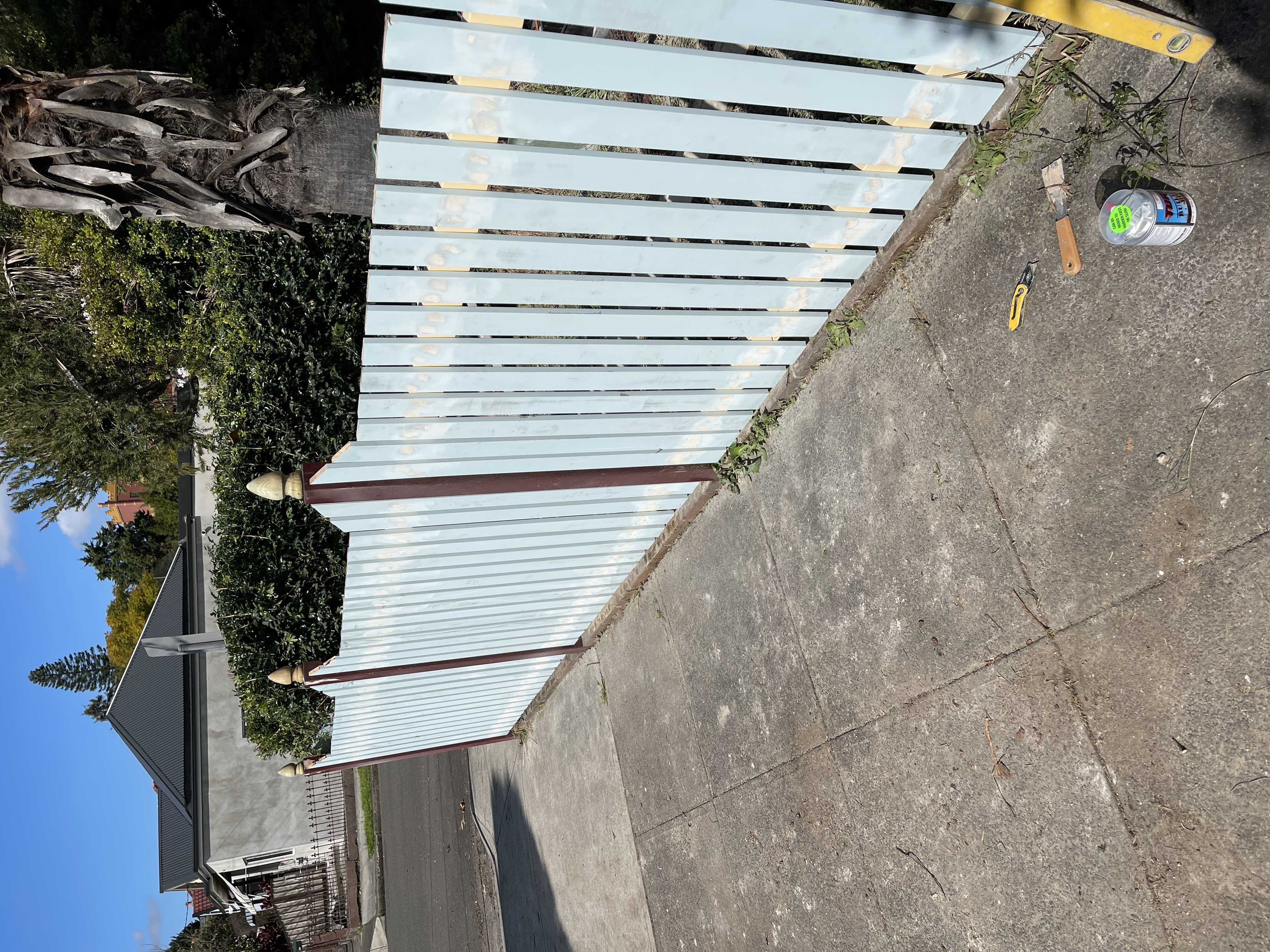 Timber picket fence with acorn finials being repainted, paint tin and tools at the base
