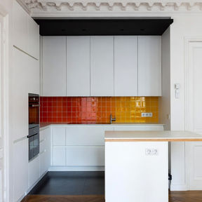 Cuisine gain de place renfoncement 90cm Paris 7e Gros-Caillou : cloison abattue, moulures restaurées, faux plafond noir, sol béton ciré gris, crédence zellige dégradé rouge orange jaune, façades blanches mates – AZ DECO 2025