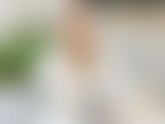     A woman in a white eyelet dress sits at an outdoor cafe table with a refreshing iced coffee, surrounded by lush greenery, exuding a relaxed and joyful vibe.