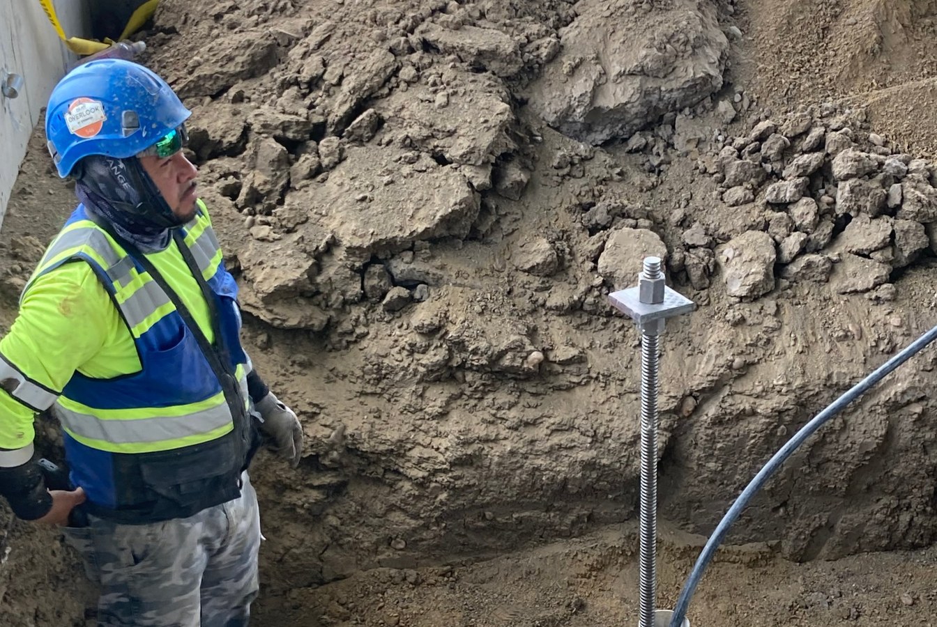Park Range crew member beside an installed micropile with its threaded top and bearing plate at Mead Fire Station No. 14