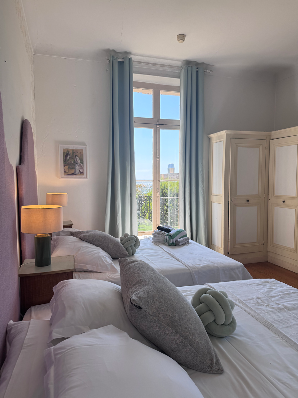 Bright hotel bedroom with two beds, purple headboard, scenic window view.