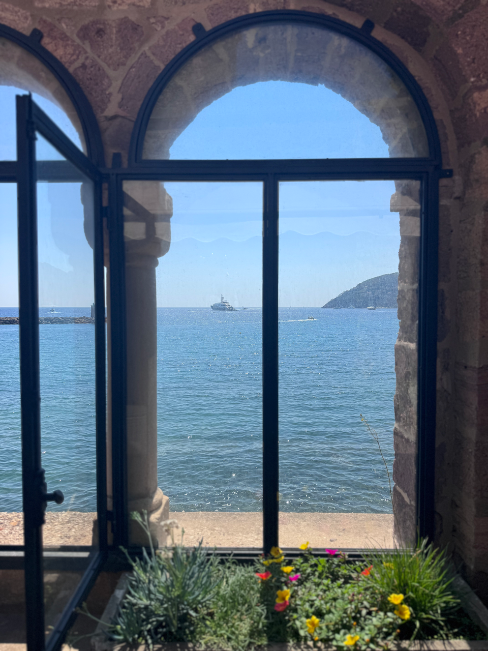 View of blue sea, distant boat through arched window; accommodations, South of France.