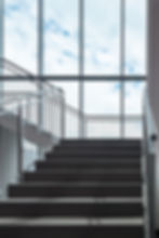 Stufen einer Stiege mit Edelstahlgeländer und einem Fenster