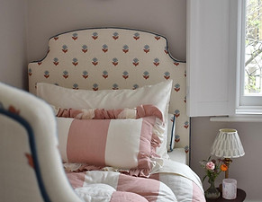 A single bed with floral headboard, pink striped linen and white solid wood shutters