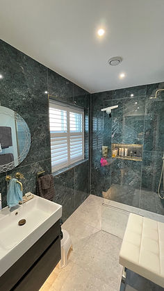 A window with vinyl shutters in a dark green marble shower room
