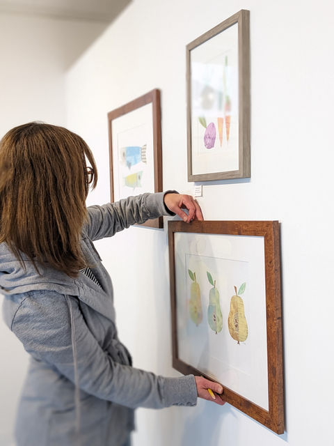 female artist hangs framed collage on an exhibit wall in a gallery