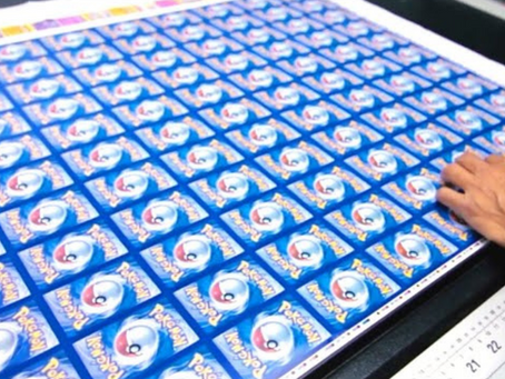A sheet of Pokémon cards being inspected during the printing process, showcasing multiple identical card backs in a vibrant blue design.