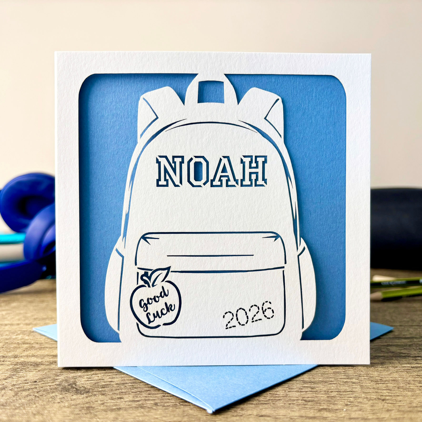 White square laser cut personalised good luck card for starting school, featuring a backpack and a pale blue paper insert.
