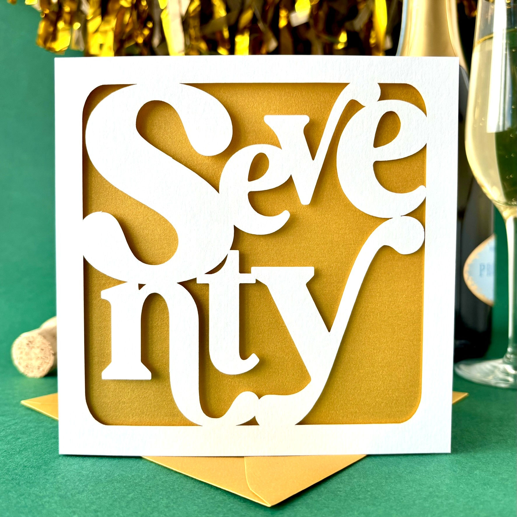 White laser cut 70th birthday card, the word 70 written in modern serif font in fun layout, with a gold paper insert.