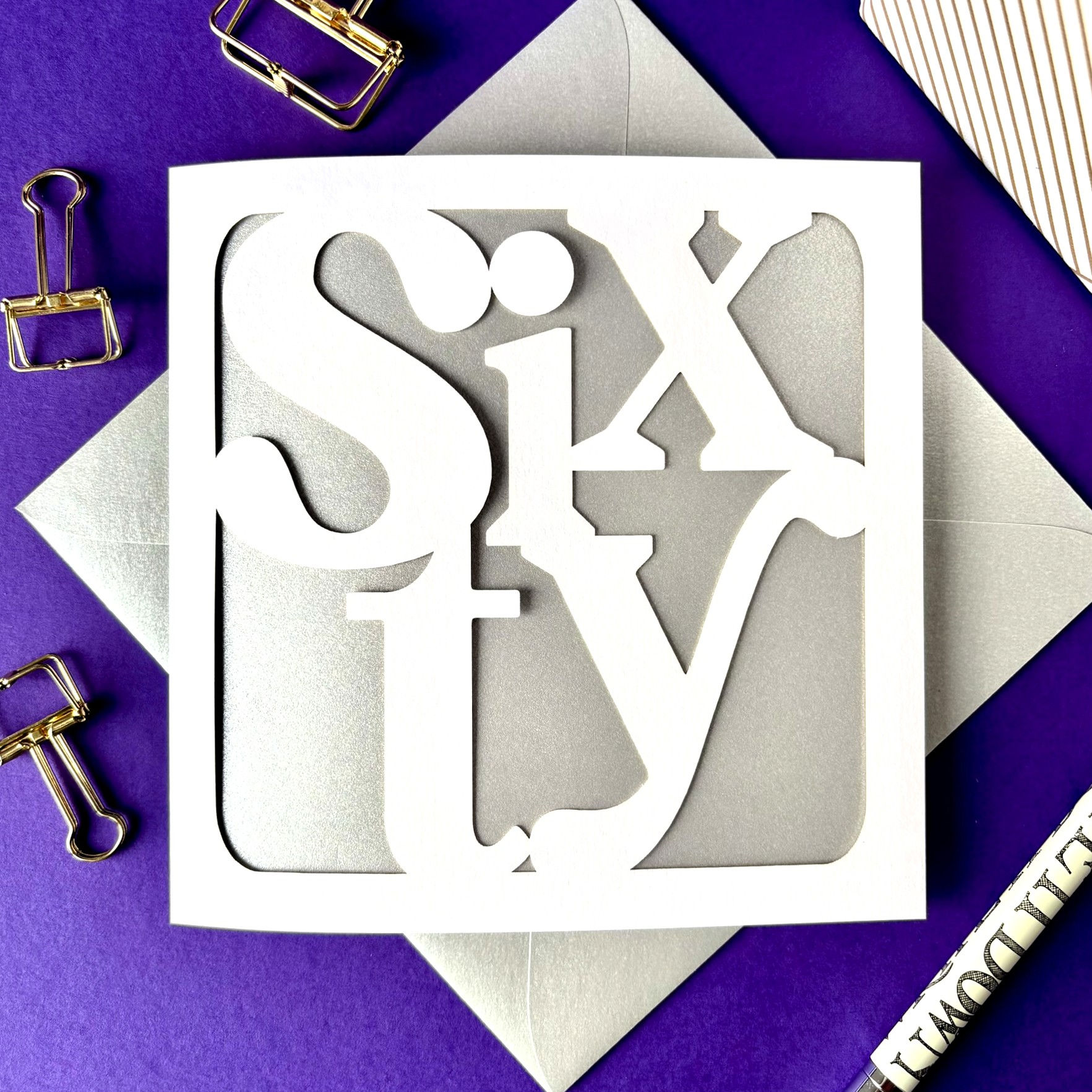 White laser cut 60th birthday card, the word 60 written in modern serif font in fun layout, with a silver paper insert.