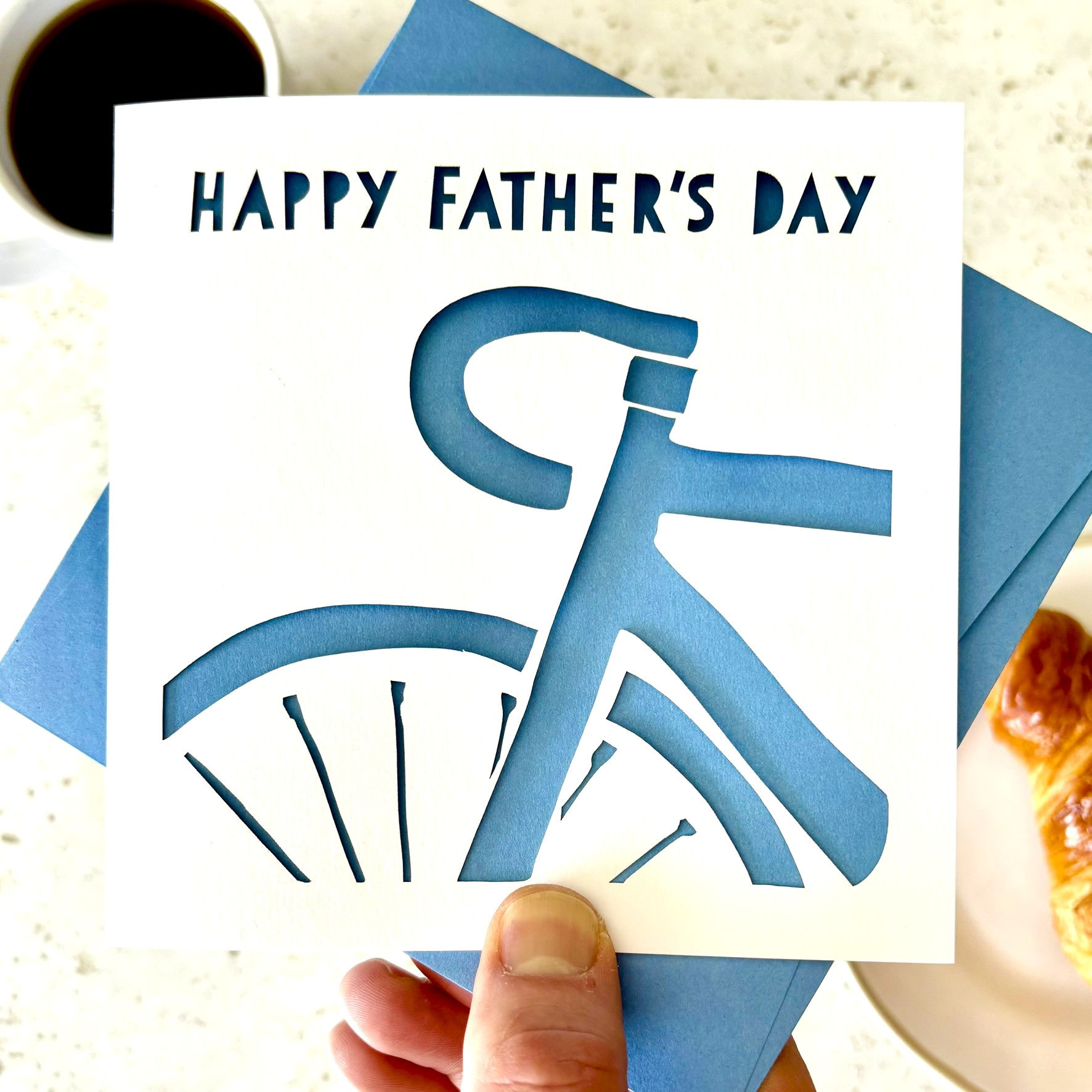 White laser cut Father's Day card, with the silhouette of a road bike cut into the card, with a blue paper insert.