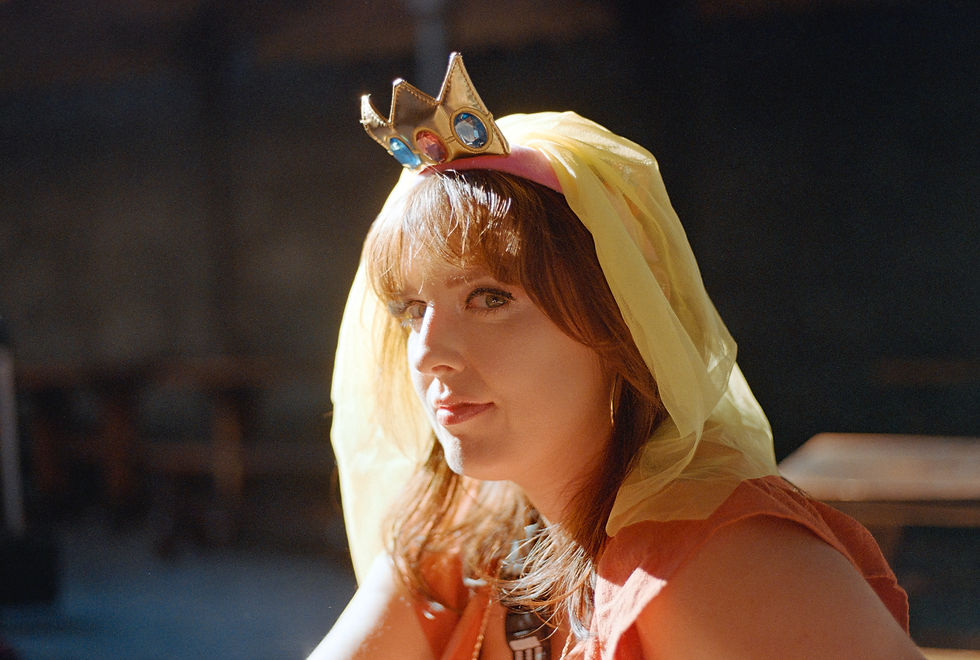 Woman wearing a jeweled crown and yellow veil, gazing thoughtfully. She's in soft indoor lighting with a blurred background. Shot on Kodak color plus film and a cheap canon film slr camera