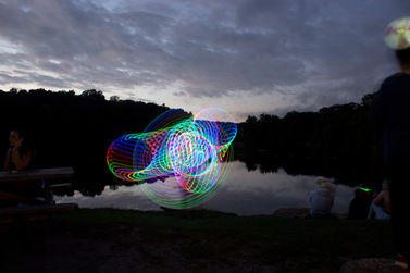 Long exposure image of a woman dancing with a rainbow LED hula hoop. The hula hoop leaves trails of light that obscure the figure. 